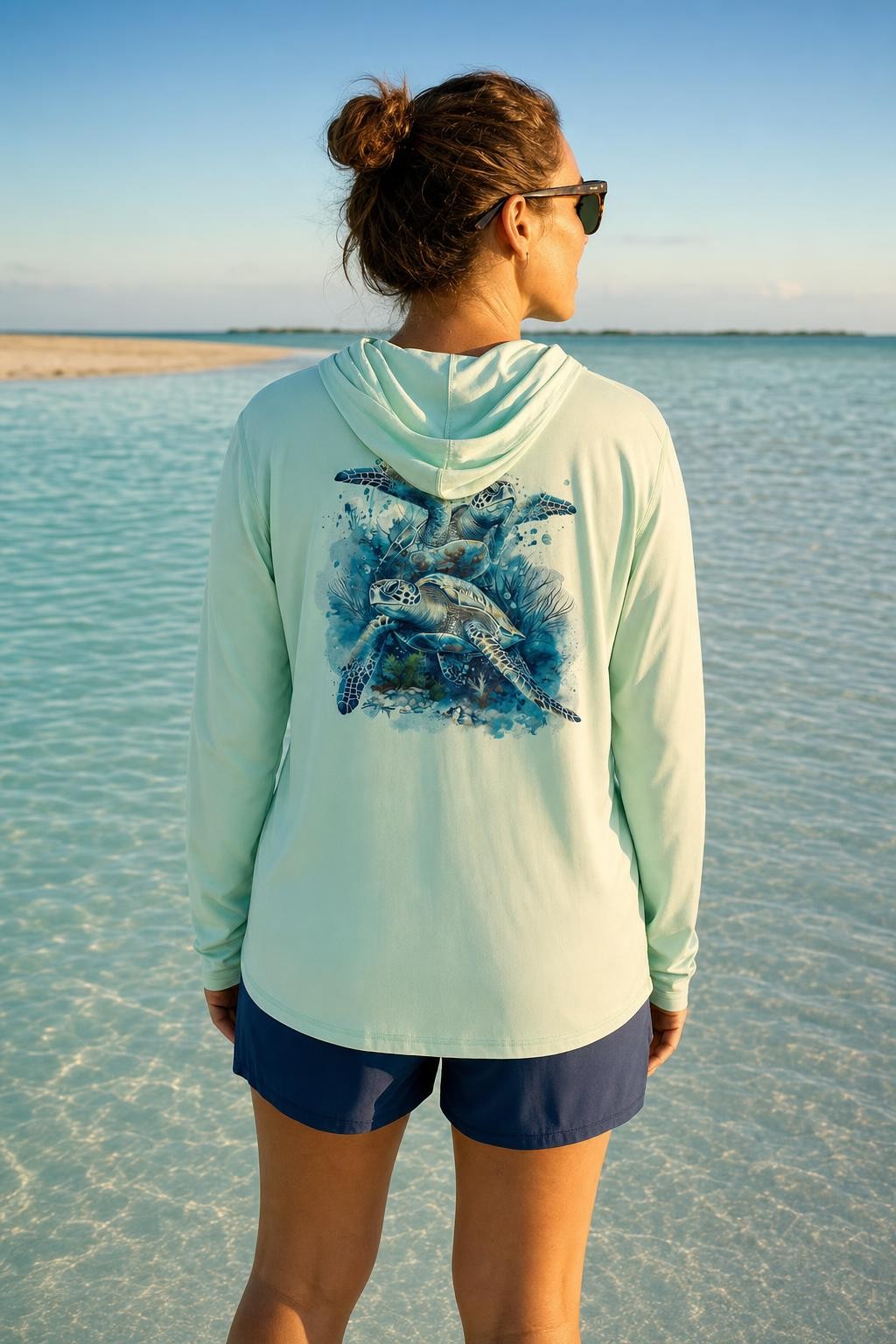 Woman on a Key West sandbar wearing the seagrass Key West Sun Shirts Sea Turtles UPF 50+ hooded sun shirt, turtle design across the back